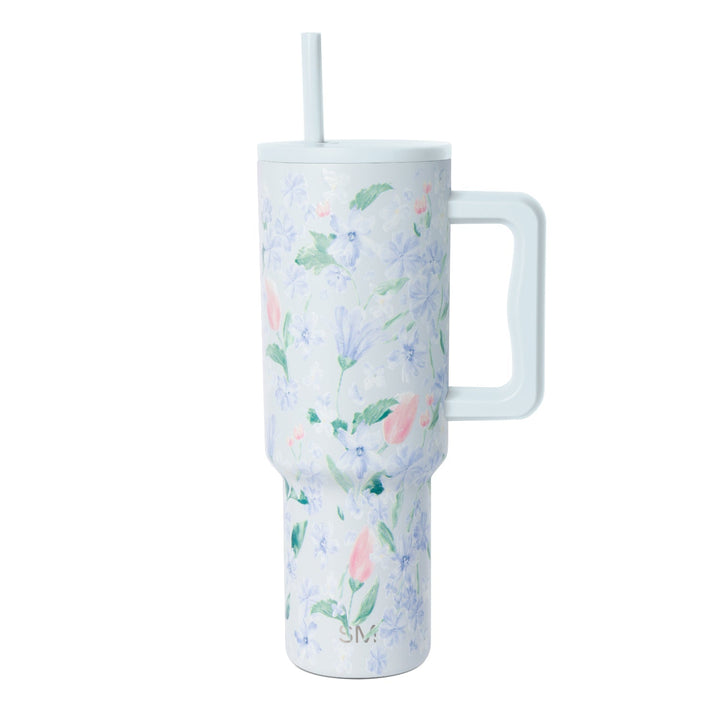 White insulated tumbler with periwinkle, lavender, and pink floral pattern, matching handle and straw, photographed against white background.